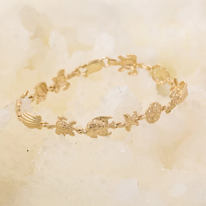 14K yellow gold bracelet with detailed ocean-themed charms including angelfish, seashells, starfish, sand dollar, and sea turtles on a soft white background.