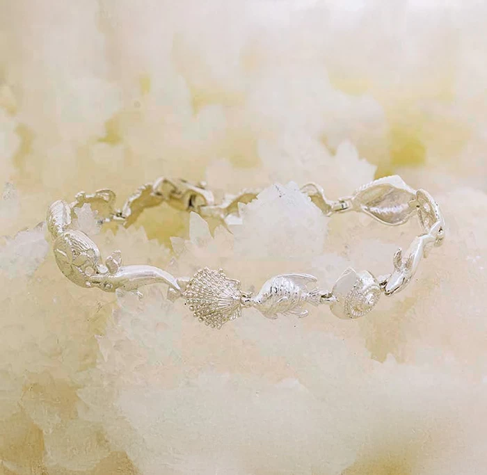 Customade white gold or silver bracelet featuring dolphin, seashell, and ocean life designs on a soft sandy background