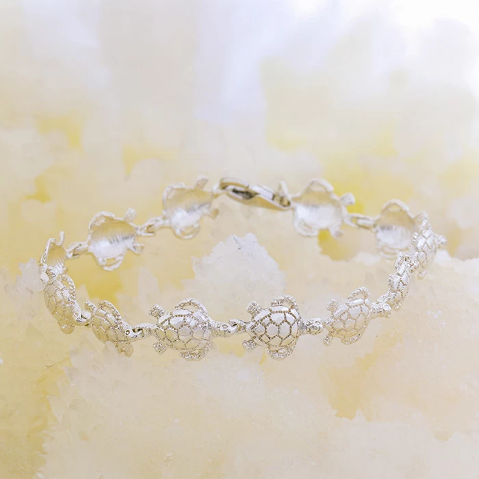 Sterling silver bracelet with detailed sea turtle links displayed on a soft, sandy-white stone background.
