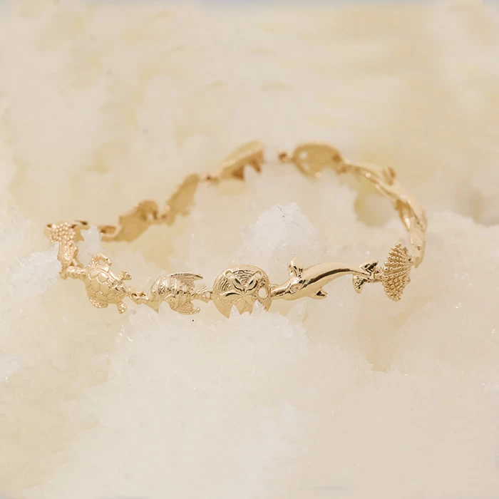 14K yellow gold bracelet with sea life charms including dolphins, turtles, clams, and angelfish on a soft white background.
